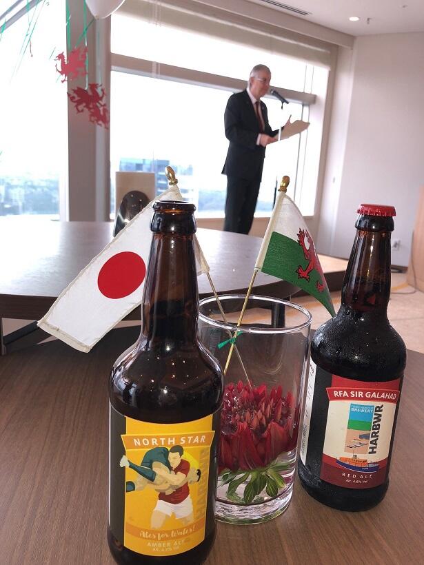 ラグビーワールドカップ2019を機会に、日本で発売されたウェールズ産のビール。左の製品には、ラグビーをテーマにしたラベルが使われている。後方は、来日したウェールズのマーク・ドレークフォード首席大臣。